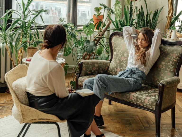 Two women engaged in a counseling session in a cozy, plant-filled living room.
