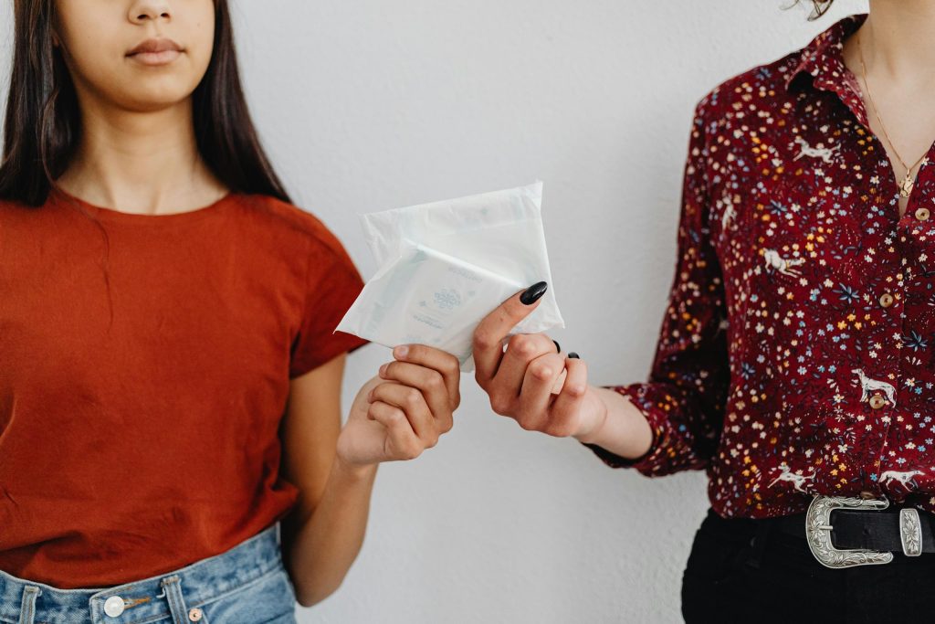 Two women exchanging sanitary pads, highlighting menstrual health awareness.