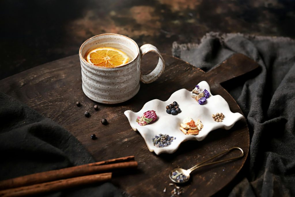 Elegant tea setting with herbal ingredients and dried orange slice on rustic tray.